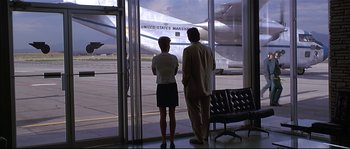 Movie still from “Con Air” (1997), directed by Simon West – A man and a woman looking out a window at an airport; Wide shot, Low angle