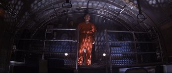 Movie still from “Con Air” (1997), directed by Simon West – A man in orange is standing on the stairs; Wide shot, Low angle