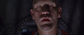 Movie still from “Con Air” (1997), directed by Simon West – A man with a shaved head is looking at the camera; Close Up shot, Low angle