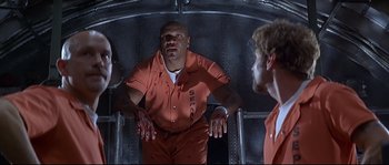 Movie still from “Con Air” (1997), directed by Simon West – Two men in orange jumpsuits in an industrial setting; Medium shot, Overhead angle
