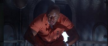 Movie still from “Con Air” (1997), directed by Simon West – A man in an orange prison uniform sitting in a doorway; Medium shot, Low angle