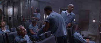 Movie still from “Con Air” (1997), directed by Simon West – A group of men in blue shirts sitting in a room; Wide shot, High angle