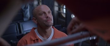 Movie still from “Con Air” (1997), directed by Simon West – A man in an orange shirt looking up at something; Close Up shot, Low angle