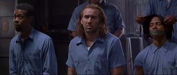 Movie still from “Con Air” (1997), directed by Simon West – A man with long hair is standing in front of a group of people; Close Up shot, Low angle