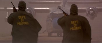 Movie still from “Con Air” (1997), directed by Simon West – Two men are standing in front of an airplane in the fog; Wide shot, Low angle