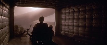 Movie still from “Con Air” (1997), directed by Simon West – A person sitting in a chair in a room; Wide shot, Low angle
