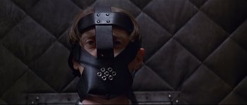 Movie still from “Con Air” (1997), directed by Simon West – A man wearing a black leather mask with a metal ring around his face; Close Up shot, Low angle