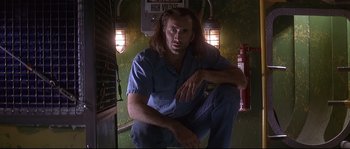 Movie still from “Con Air” (1997), directed by Simon West – A man sitting on the floor in a room; Medium shot, Low angle