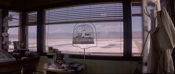 Movie still from “Con Air” (1997), directed by Simon West – A bird in a cage in front of a large window; Wide shot, Low angle
