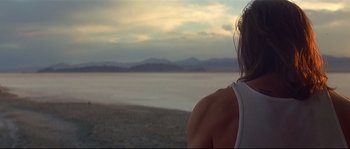 Movie still from “Con Air” (1997), directed by Simon West – A woman standing on the beach looking out at the ocean; Medium shot, Over the shoulder angle