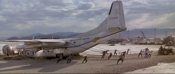 Movie still from “Con Air” (1997), directed by Simon West – A group of people are walking around an airplane on the ground; Extreme Wide shot, Low angle