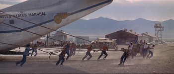 Movie still from “Con Air” (1997), directed by Simon West – A group of people are pulling a plane on a rope; Extreme Wide shot, Low angle