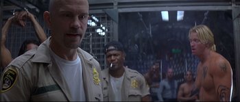 Movie still from “Con Air” (1997), directed by Simon West – A man in a uniform smoking a cigarette in front of a group of people; Close Up shot, Low angle