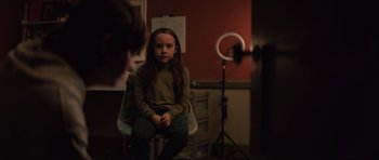 Movie still from “The Boogeyman” (2023), directed by Rob Savage – A girl sitting in a chair in front of a ring light; Medium shot, Over the shoulder angle