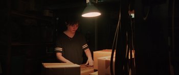 Movie still from “The Boogeyman” (2023), directed by Rob Savage – A person standing in front of boxes under a lamp; Medium shot, Over the shoulder angle