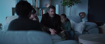 Movie still from “The Boogeyman” (2023), directed by Rob Savage – A man sitting on top of a couch next to a child; Medium shot, Over the shoulder angle