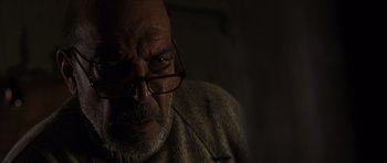 Movie still from “The Bourne Identity” (2002), directed by Doug Liman – An older man wearing glasses and a sweater looking at the camera; Close Up shot, Low angle