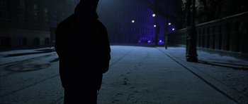 Movie still from “The Bourne Identity” (2002), directed by Doug Liman – A person standing on a snowy sidewalk at night; Wide shot, Over the shoulder angle