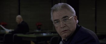 Movie still from “The Bourne Identity” (2002), directed by Doug Liman – An older man wearing glasses and a suit; Close Up shot, Low angle
