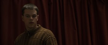 Movie still from “The Bourne Identity” (2002), directed by Doug Liman – A man wearing a sweater standing in front of a red curtain; Close Up shot, Low angle