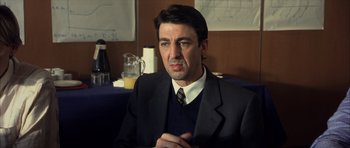 Movie still from “The Bourne Identity” (2002), directed by Doug Liman – A man wearing a suit and tie sitting in front of a wall; Close Up shot, Over the shoulder angle