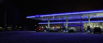 Movie still from “The Bourne Identity” (2002), directed by Doug Liman – Cars parked at a gas station at night with blue lights; Extreme Wide shot, Low angle