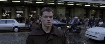 Movie still from “The Bourne Identity” (2002), directed by Doug Liman – A man in a brown jacket standing in front of a crowd of onlookers; Close Up shot, Low angle