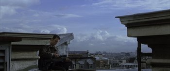 Movie still from “The Bourne Identity” (2002), directed by Doug Liman – A man sitting on top of a building looking at his cell phone; Wide shot, Low angle
