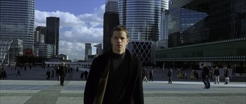 Movie still from “The Bourne Identity” (2002), directed by Doug Liman – A man in a black jacket standing in front of a building; Medium shot, Low angle