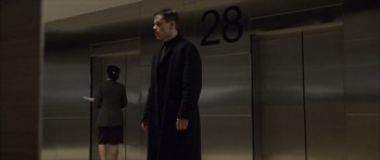 Movie still from “The Bourne Identity” (2002), directed by Doug Liman – A man in a black coat standing in front of an elevator; Wide shot, Low angle