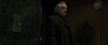 Movie still from “The Bourne Identity” (2002), directed by Doug Liman – An older man wearing a black coat and glasses; Medium shot, Low angle