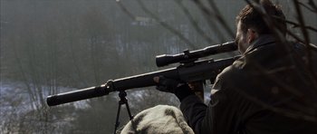 Movie still from “The Bourne Identity” (2002), directed by Doug Liman – A man holding a rifle with a scope on it; Medium shot, Over the shoulder angle
