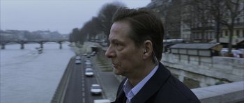 Movie still from “The Bourne Identity” (2002), directed by Doug Liman – A man in a suit and ear buds standing on the side of a road; Close Up shot, Over the shoulder angle