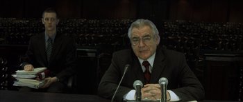 Movie still from “The Bourne Identity” (2002), directed by Doug Liman – An older man in a black suit and red neck tie; Medium shot, Over the shoulder angle
