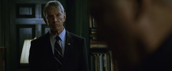 Movie still from “The Bourne Legacy” (2012), directed by Tony Gilroy – A man in a suit and tie standing in front of a bookshelf; Close Up shot, Over the shoulder angle