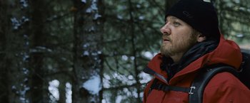 Movie still from “The Bourne Legacy” (2012), directed by Tony Gilroy – A man in a red jacket standing next to a tree; Close Up shot, Low angle