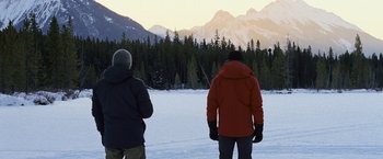 Movie still from “The Bourne Legacy” (2012), directed by Tony Gilroy – Two people standing in the snow looking out at the mountains; Wide shot, Over the shoulder angle