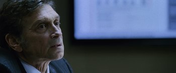 Movie still from “The Bourne Legacy” (2012), directed by Tony Gilroy – An older man sitting in front of a television; Close Up shot, Over the shoulder angle