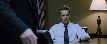 Movie still from “The Bourne Legacy” (2012), directed by Tony Gilroy – A man sitting in front of an american flag; Medium shot, Low angle