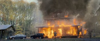Movie still from “The Bourne Legacy” (2012), directed by Tony Gilroy – A man standing in front of a house on fire; Extreme Wide shot, Low angle