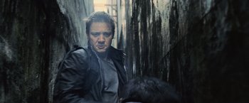 Movie still from “The Bourne Legacy” (2012), directed by Tony Gilroy – A man in black jacket standing in front of trees; Close Up shot, Low angle