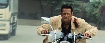 Movie still from “The Bourne Legacy” (2012), directed by Tony Gilroy – A man riding a motorcycle on the side of the road; Medium shot, Low angle