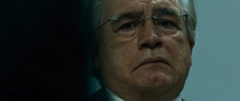 Movie still from “The Bourne Supremacy” (2004), directed by Paul Greengrass – An older man wearing glasses and a suit and tie; Close Up shot, Low angle