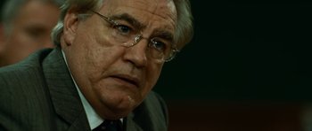 Movie still from “The Bourne Supremacy” (2004), directed by Paul Greengrass – An older man wearing glasses and wearing a suit; Close Up shot, Over the shoulder angle