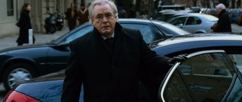Movie still from “The Bourne Supremacy” (2004), directed by Paul Greengrass – An older man wearing a suit and tie walking next to a car; Medium shot, Over the shoulder angle