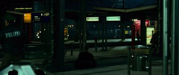 Movie still from “The Bourne Supremacy” (2004), directed by Paul Greengrass – A man sitting on the side of a train platform at night; Extreme Wide shot, High angle
