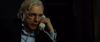 Movie still from “The Bourne Supremacy” (2004), directed by Paul Greengrass – An older man talking on a phone while wearing glasses; Close Up shot, Over the shoulder angle