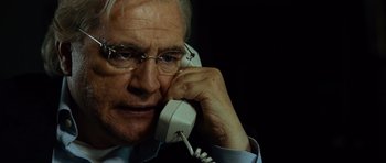 Movie still from “The Bourne Supremacy” (2004), directed by Paul Greengrass – An older man talking on a phone while wearing glasses; Close Up shot, Over the shoulder angle
