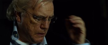 Movie still from “The Bourne Supremacy” (2004), directed by Paul Greengrass – An older man wearing glasses and a suit; Close Up shot, Over the shoulder angle