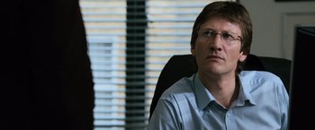 Movie still from “The Bourne Ultimatum” (2007), directed by Paul Greengrass – A man sitting at a desk in an office chair; Close Up shot, Over the shoulder angle